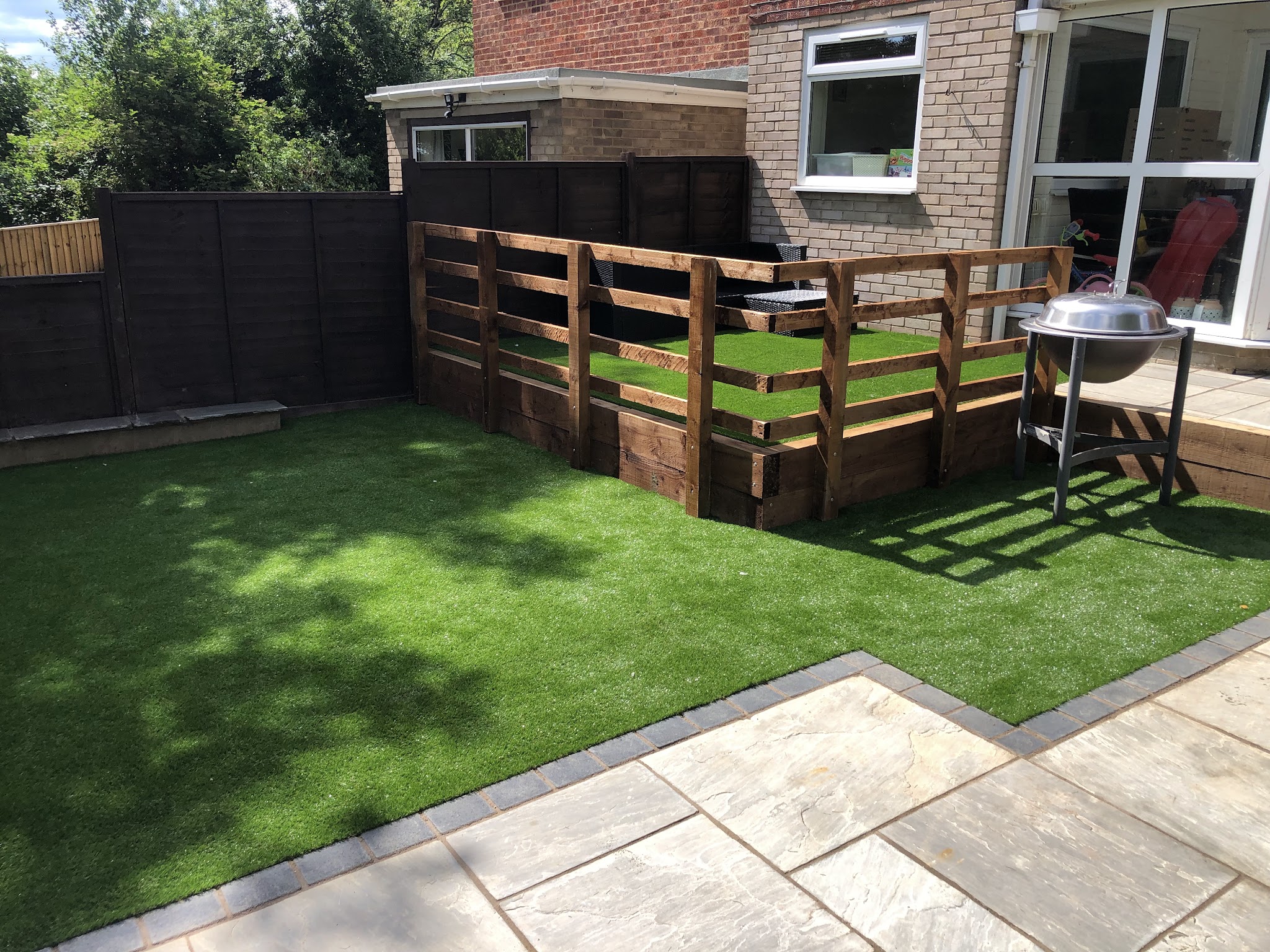 Artificial lawn edged with an Indian sandstone patio and a low timber fence